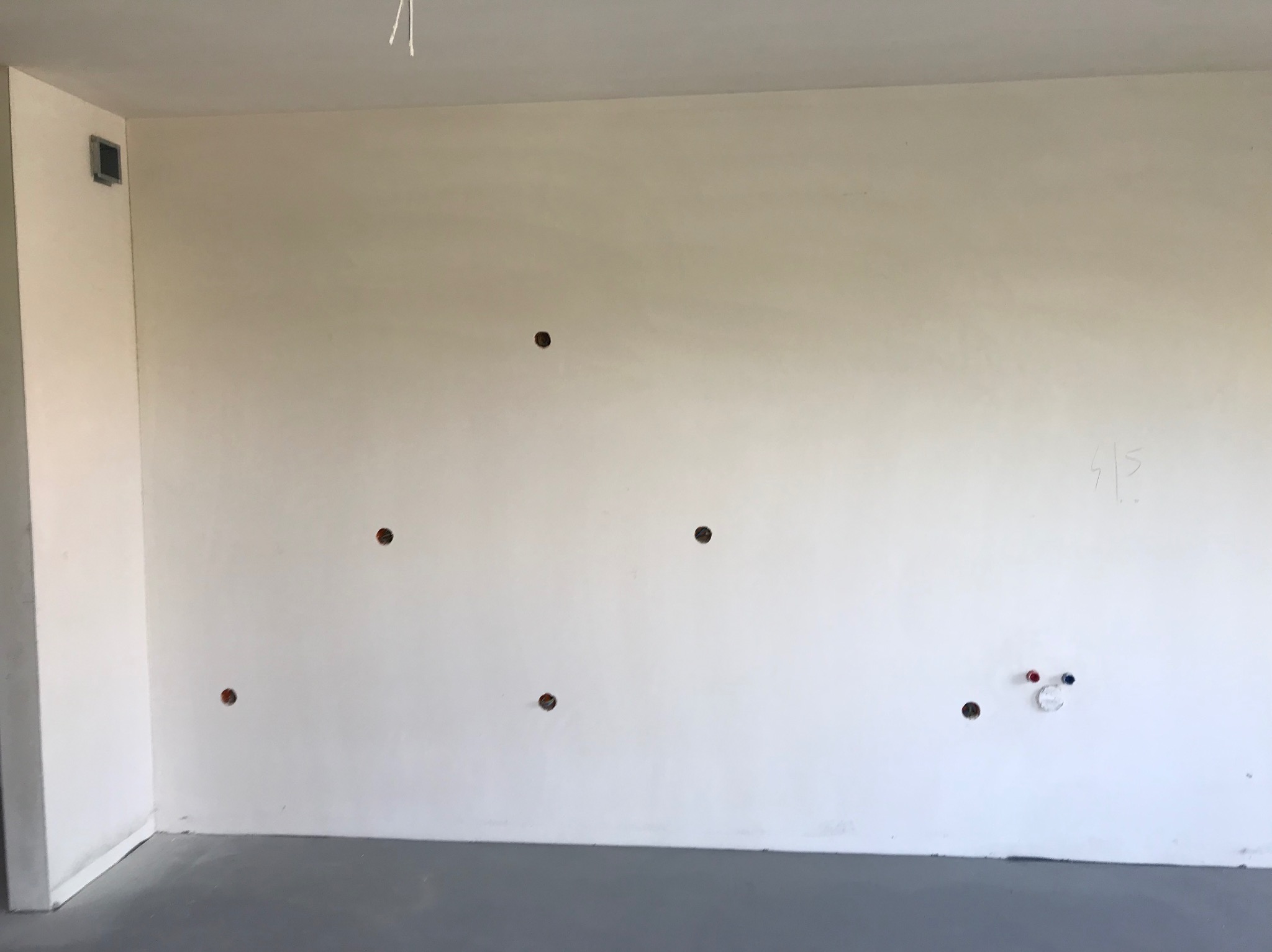 Ściana z wywierconymi otworami pod instalacje elektryczne i wodne w nowym budynku. Szare podłoże, minimalistyczne wnętrze, surowy stan wykończenia.