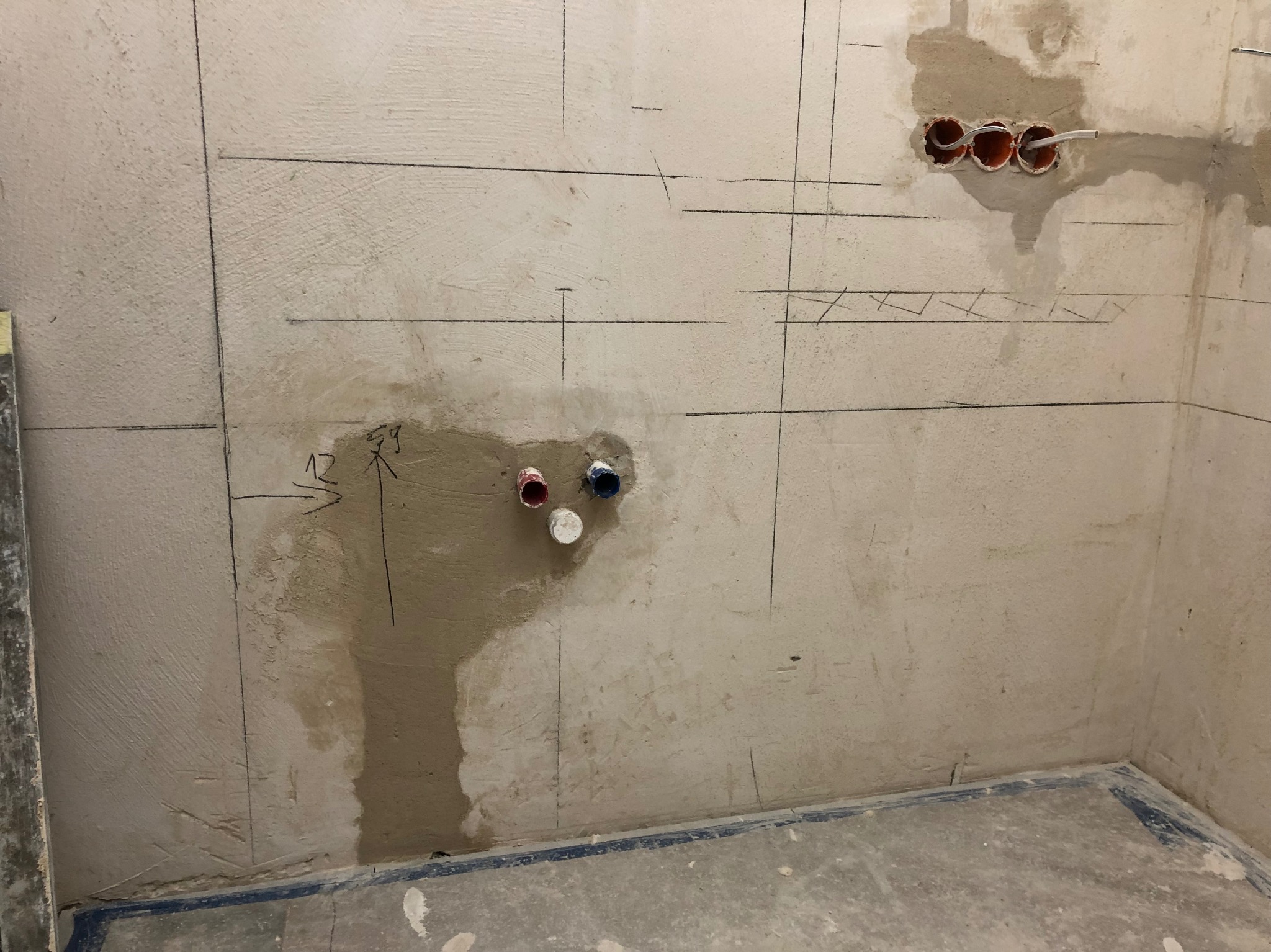 Ściana w trakcie prac instalacyjnych: wyznaczone linie, otwory na kable i rury, widoczne przewody. Etap przygotowania do dalszych prac wykończeniowych w pomieszczeniu.