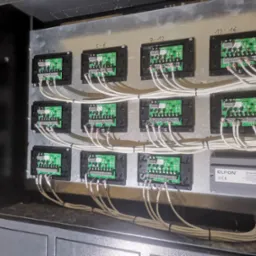 Rozdzielnica z modułami komunikacyjnymi ElfON, widoczne przewody i złącza. Instalacja w szafie, z bliska, z numeracją modułów.