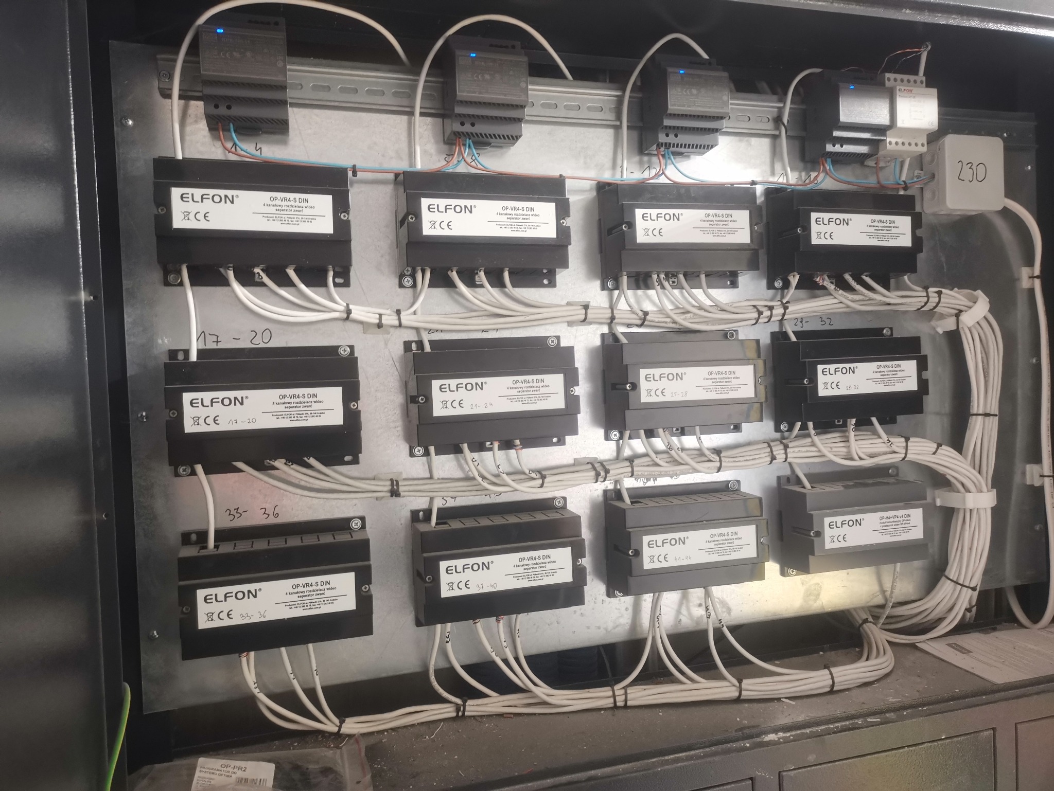 Rozdzielnica z zamontowanymi modułami marki Elfon OP-VR4-S DIN i przewodami. Widoczne opisy numeracji przewodów. Instalacja telekomunikacyjna w szarej obudowie.