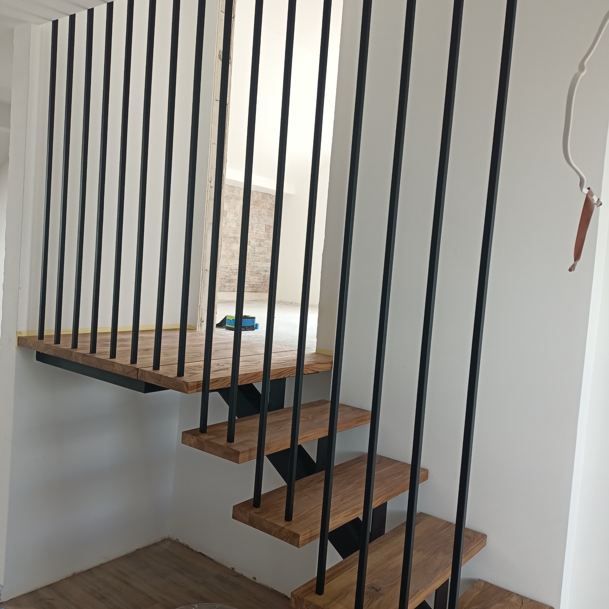 Nowoczesne schody z drewnianymi stopniami i czarnymi, pionowymi elementami balustrady. Widok z dołu na jasne wnętrze w tle. Minimalistyczny design.