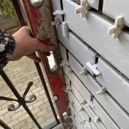 PAT-BUD - Układanie białych płytek na balkonie z użyciem krzyżyków dystansowych, sprawdzane poziomicą. Widoczne barierki balkonu i fragment podłogi.