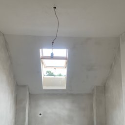 PAT-BUD - Pokój ze ścianami po szpachlowaniu, widoczne okno dachowe i wystający kabel z sufitu. Przygotowanie do dalszych prac wykończeniowych.