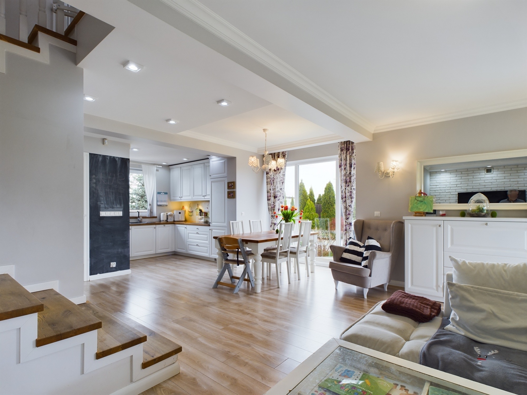 Jasne wnętrze: schody, parkiet, kuchnia z oknem na ogród, stół jadalny i salon z kanapą. Przestronne, nowoczesne mieszkanie.
