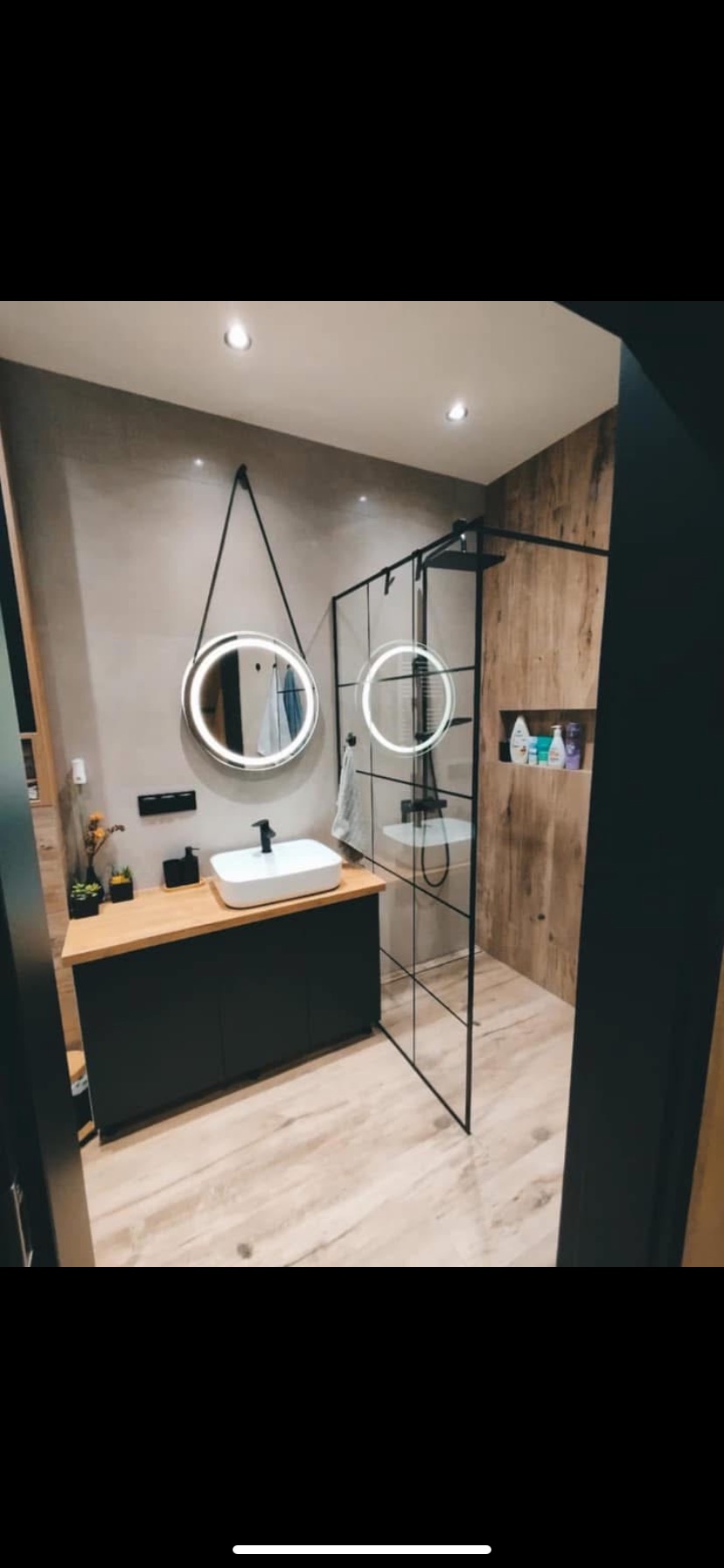 Nowoczesna łazienka z kabiną typu walk-in, okrągłym lustrem z podświetleniem LED i drewnianymi akcentami na ścianach. Minimalistyczny design.