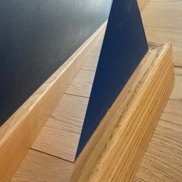 Wood Vibes Only - Szczegółowe ujęcie drewnianej listwy przypodłogowej, łączącej się z ciemną ścianą i drewnianą podłogą. Widoczne detale wykończenia i połączenia materiałów.