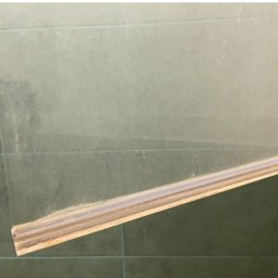 Angelika Kowal - Brudna szyba okienna z drewnianą ramą, widoczne zacieki i osad, na tle zielonych płytek. Wymaga czyszczenia, zbliżenie na dolną część okna.