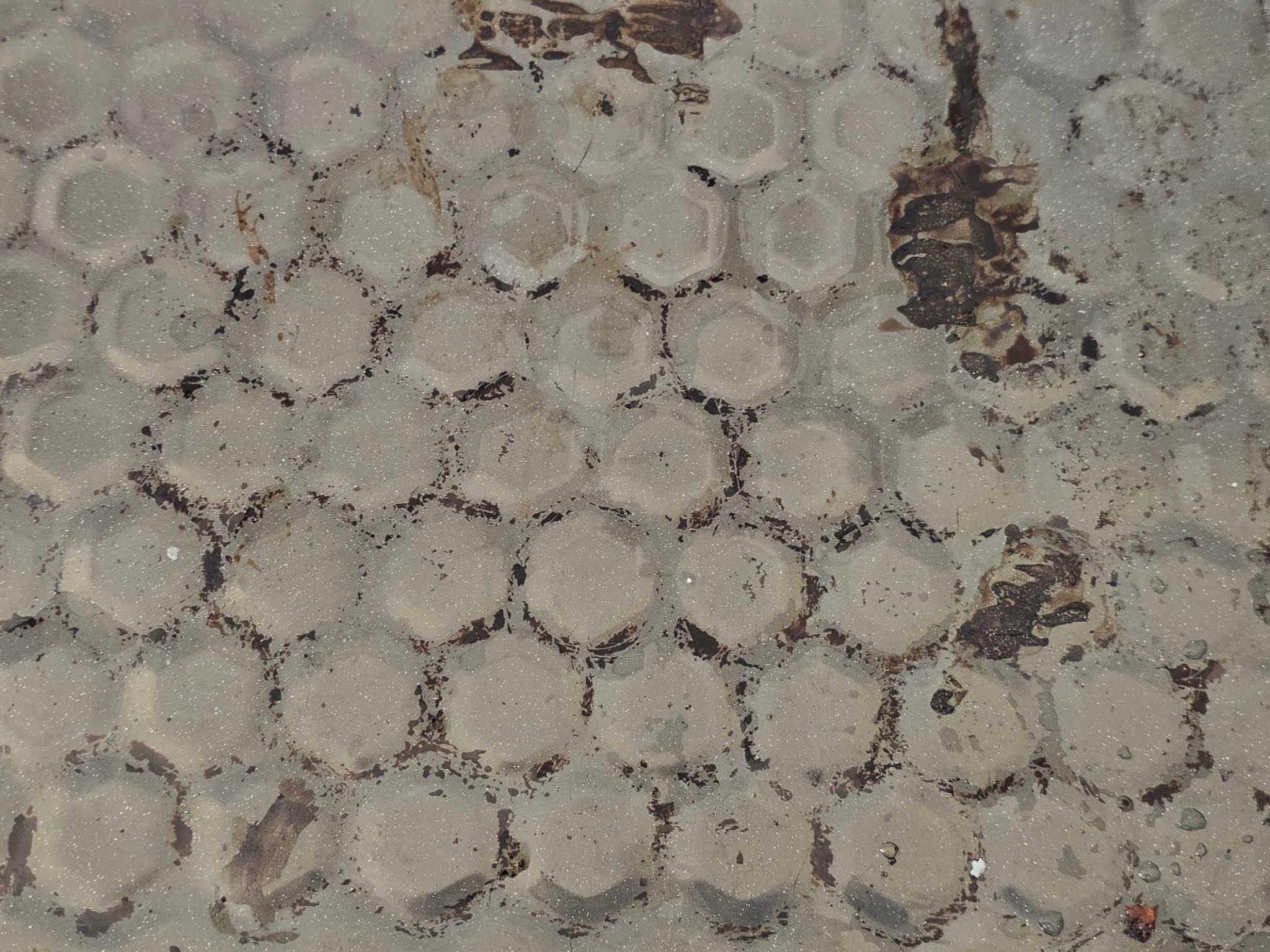 Silnie zabrudzona, szara powierzchnia z sześciokątnym wzorem. Widoczne plamy błota i zaschniętych zabrudzeń. Powierzchnia wymaga gruntownego czyszczenia.