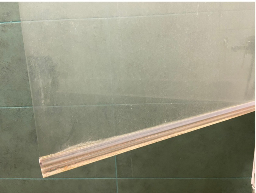 Brudna szyba okienna z drewnianą ramą, widoczne zacieki i osad, na tle zielonych płytek. Wymaga czyszczenia, zbliżenie na dolną część okna.