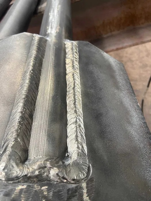 Szlifowana powierzchnia metalowa z wyraźnymi, precyzyjnymi spawami wzdłuż krawędzi, ukazująca detale łączenia elementów konstrukcyjnych.