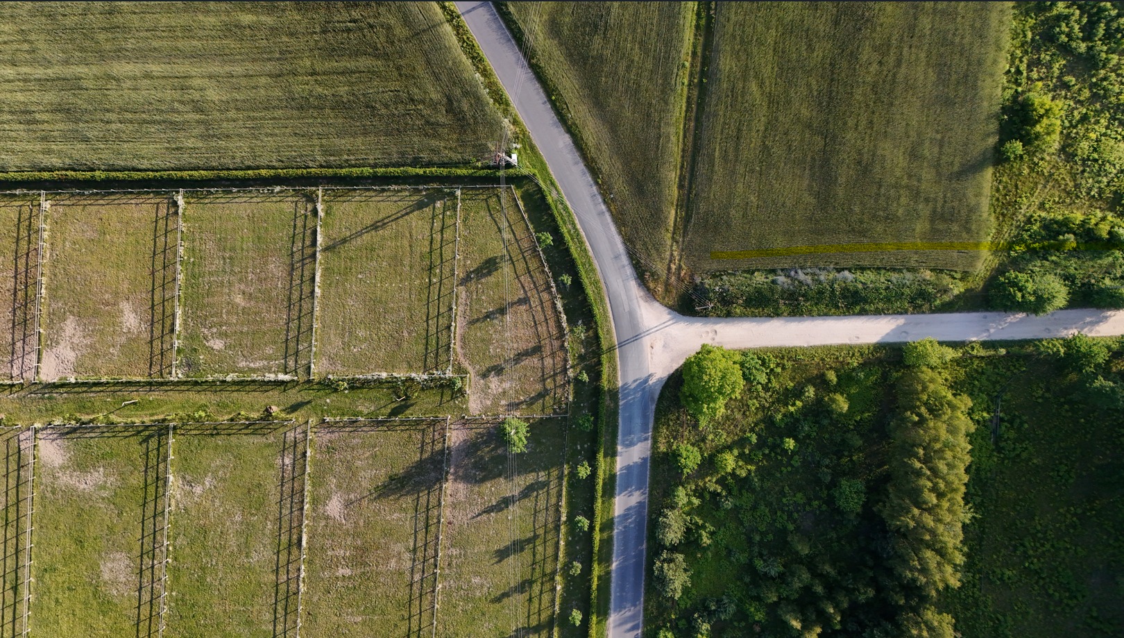 Zdjęcie z drona: skrzyżowanie dróg polnych, pola uprawne i pastwiska z ogrodzeniami. Widok z góry, równomierne oświetlenie, wyraźne linie podziału pól.