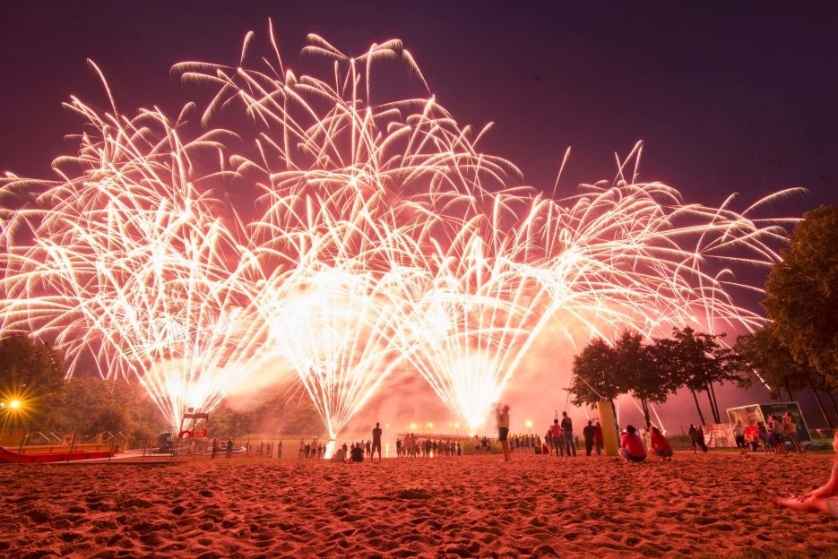 Spektakularny pokaz fajerwerków nad plażą w Gądkach, z sylwetkami widzów na tle nocnego nieba rozświetlonego przez wybuchające sztuczne ognie.