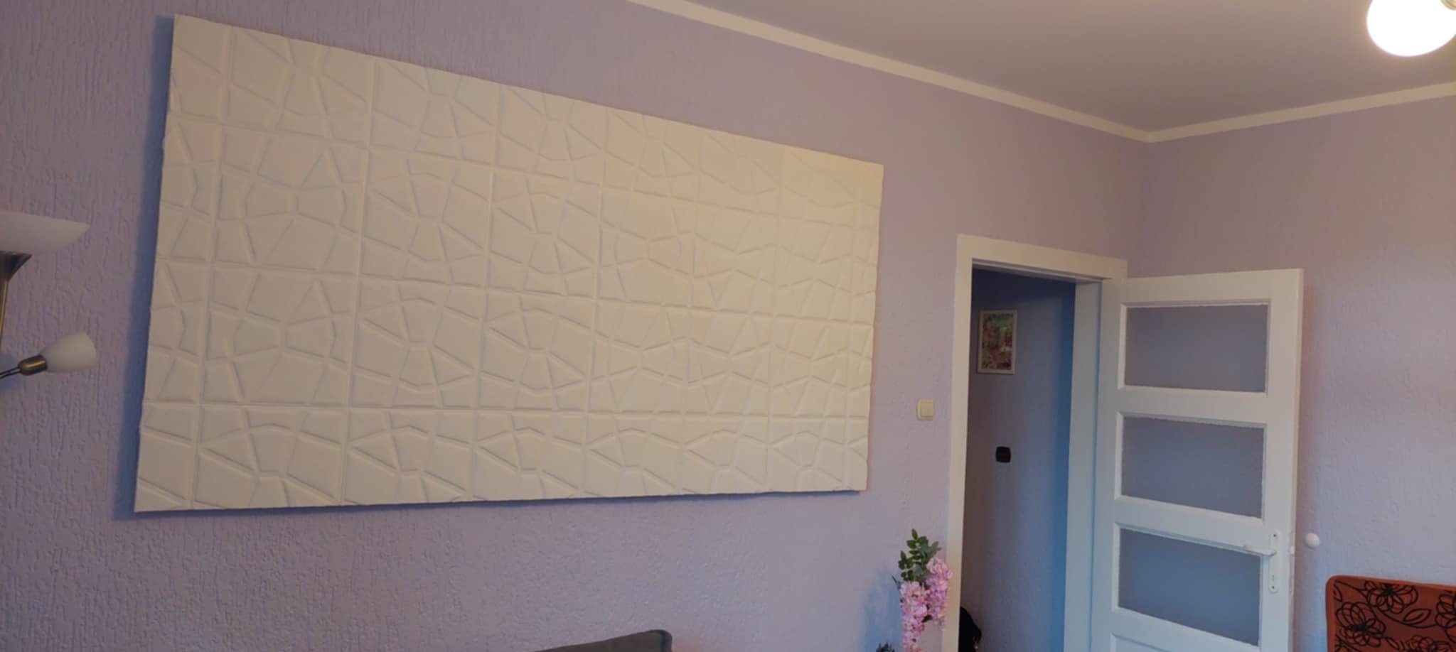 Panel 3D na fioletowej ścianie w pokoju. Dekoracyjny element z geometrycznym wzorem. Widoczny fragment drzwi i lampy.