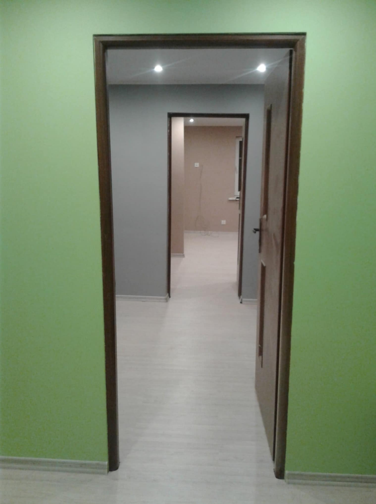 Pomalowane na jasno ściany mieszkania po remoncie, widok z korytarza przez otwarte drzwi do kolejnych pomieszczeń. Świeże, pastelowe kolory.