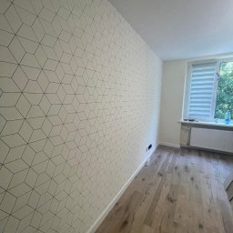 UKAL Remonty Łukasz Leśniewski - Pokój po remoncie: geometryczna tapeta na ścianie, drewniana podłoga, okno z żaluzjami. Jasne wnętrze z nowoczesnym designem.