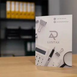 Karta wizytowa firmy Lusitax na biurku, z kalkulatorem, lupą i spinaczami. W tle regał z segregatorami. Kontakt: +48 794 294 634, kontakt@lusitax.pl.