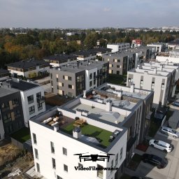 Videofilmowanie Anna Kusiak - Zdjęcie z drona przedstawia osiedle nowoczesnych, wielopiętrowych budynków z płaskimi dachami i zielonymi tarasami. Widoczne zaparkowane samochody i drzewa w tle.