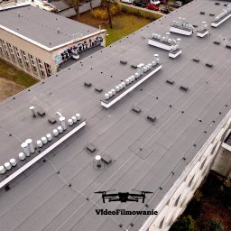Videofilmowanie Anna Kusiak - Zdjęcie z drona przedstawia płaski dach budynku z licznymi kominami wentylacyjnymi i instalacjami. Na dachu widoczne logo firmy 'VideoFilmowanie'.