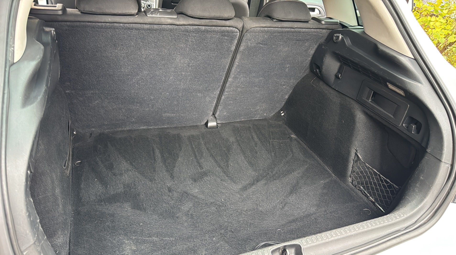 Wyprana tapicerka bagażnika samochodu, widoczne ślady po czyszczeniu na ciemnej wykładzinie. Siatka w bocznej części bagażnika.
