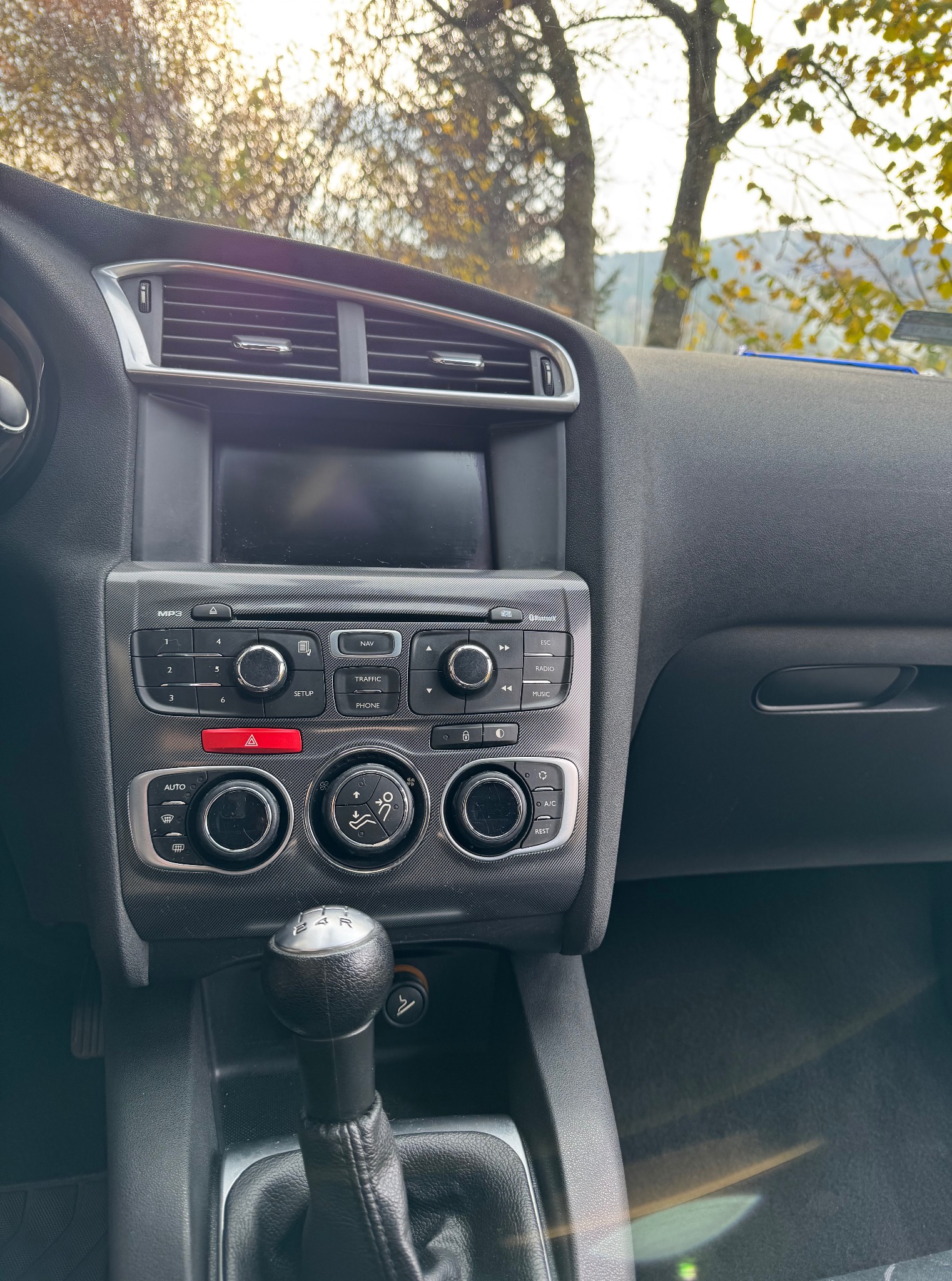 Wnętrze samochodu z widocznym kokpitem, konsolą środkową i dźwignią zmiany biegów. Widoczne elementy sterowania klimatyzacją i systemem audio.