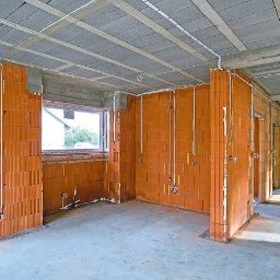 EcoVolt - Surowy stan wnętrza domu w trakcie budowy: ceglane ściany z widoczną instalacją elektryczną w białych rurkach, betonowy strop, okna.