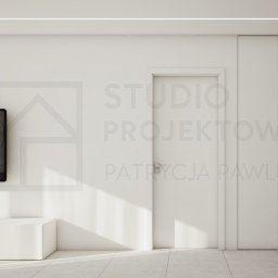 Studio Projektowe Patrycja Pawlus - Minimalistyczny salon z białymi meblami i telewizorem na ścianie. Proste linie, stonowana kolorystyka i subtelne oświetlenie tworzą nowoczesną przestrzeń.