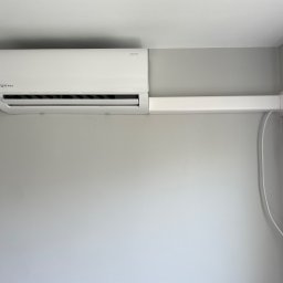 MAGELECTRIC - Biały klimatyzator Rotenso zamontowany na szarej ścianie, z widoczną listwą maskującą przewody. Minimalistyczny design, nowoczesne wnętrze.
