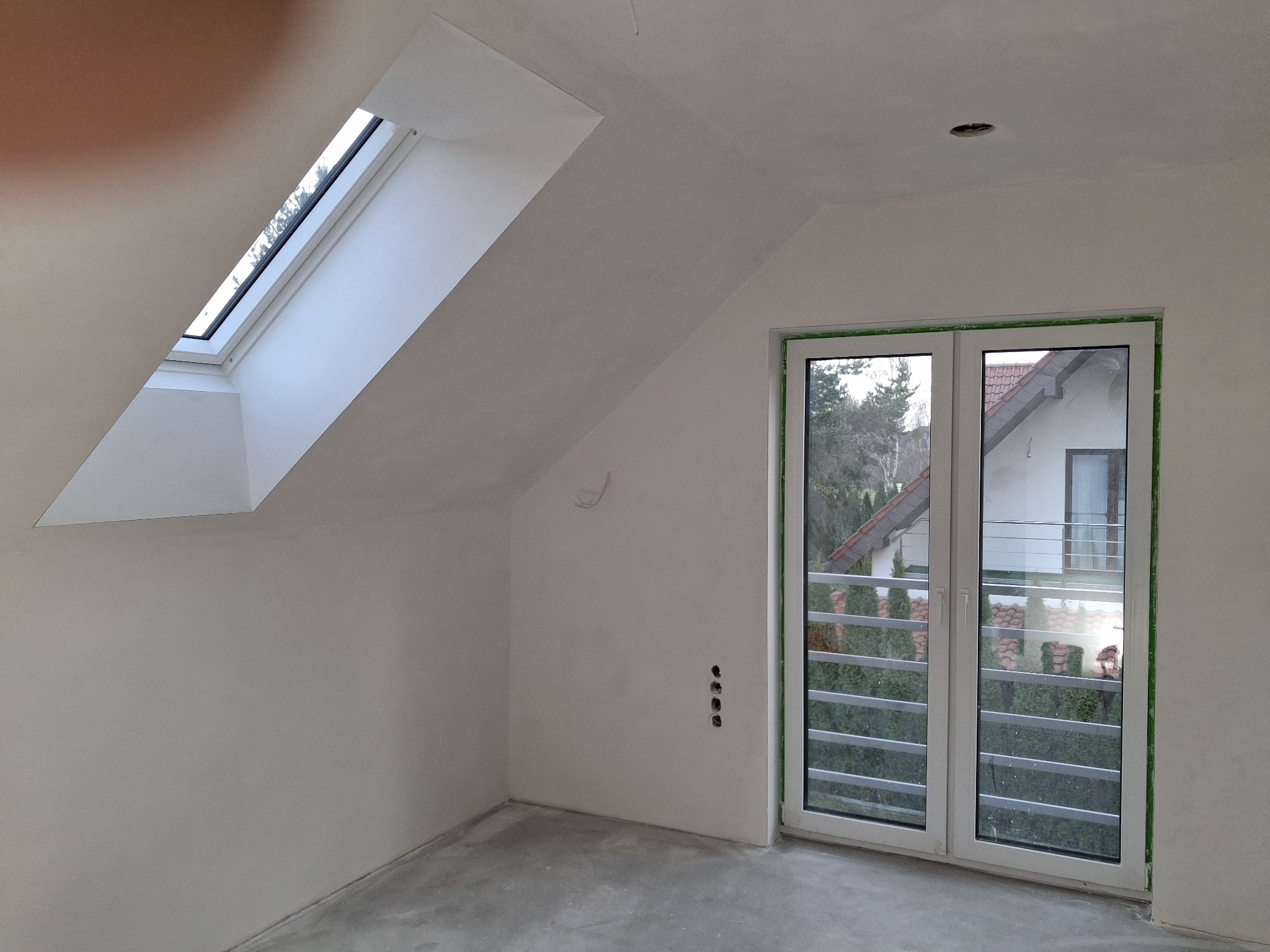 Poddasze po szpachlowaniu: okno dachowe, drzwi balkonowe z widokiem na zewnątrz, ściany przygotowane do malowania, widoczne puszki elektryczne.