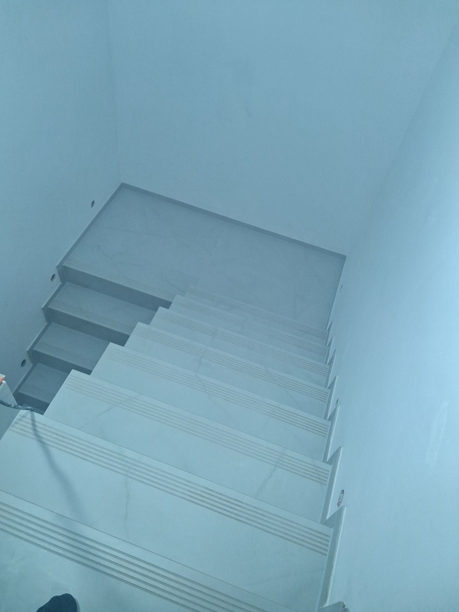 Wykończone schody wewnątrz budynku, pokryte jasnymi płytkami z delikatnym wzorem. Widok z góry, ukazujący detale wykończenia i minimalistyczny design.