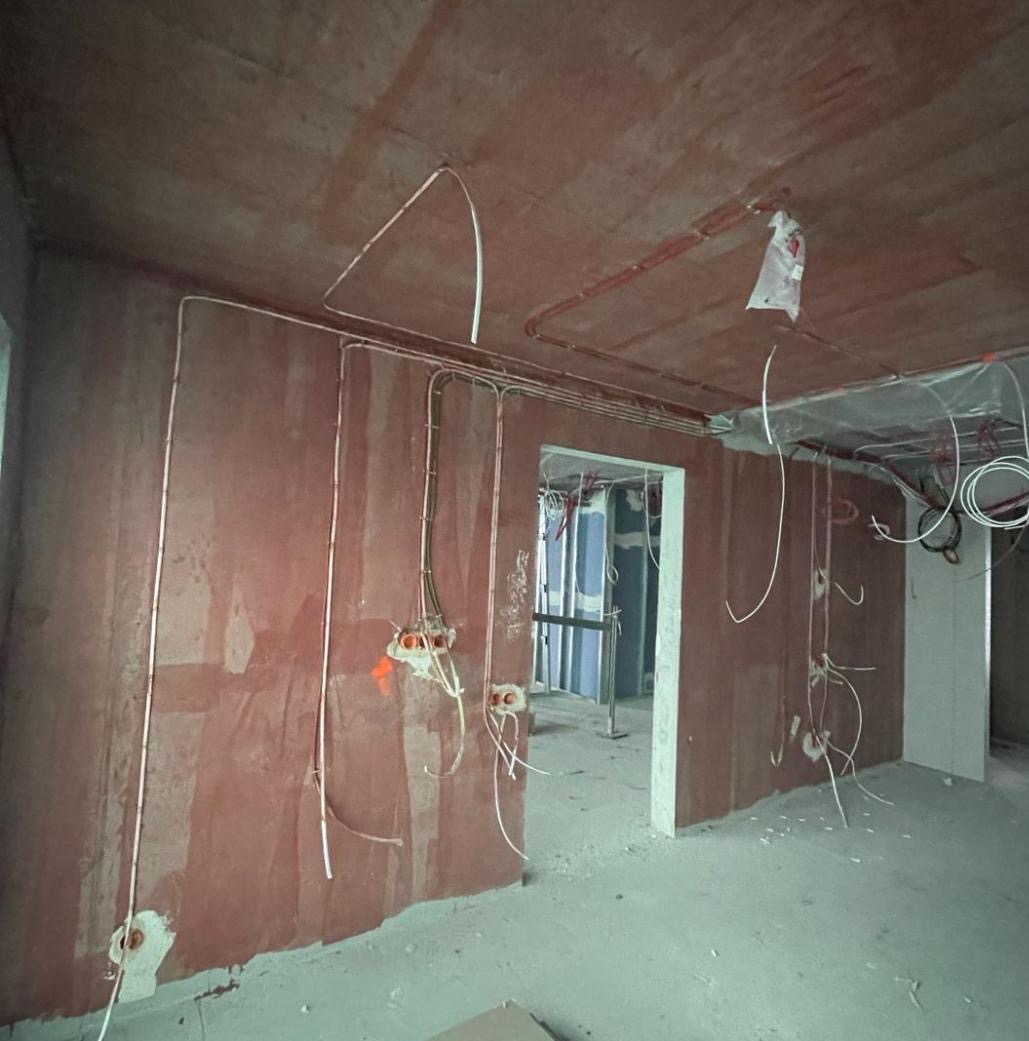 Wnętrze w trakcie prac elektrycznych: kable prowadzone po ścianach i suficie, puszki instalacyjne. Surowy stan wykończenia, widok na kolejne pomieszczenie.