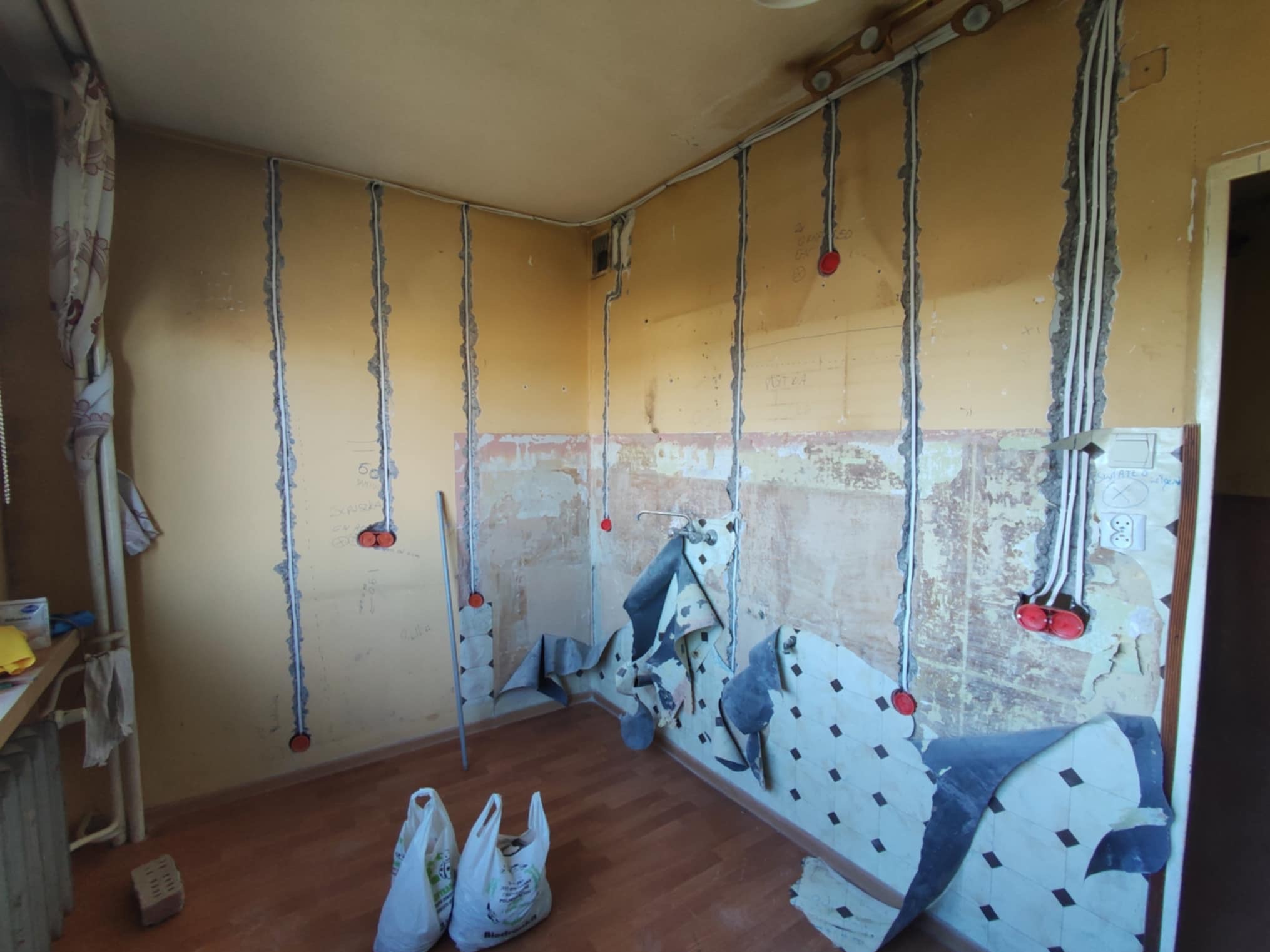 Remont kuchni: bruzdy w ścianach pod instalacje elektryczne, widoczne kable w peszlach. Częściowo zerwane stare płytki. Przygotowanie do położenia nowej instalacji.
