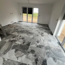 Ułożona podłoga z płytek imitujących marmur w jasnym pokoju z dużymi oknami balkonowymi. Widoczne fragmenty drabiny.