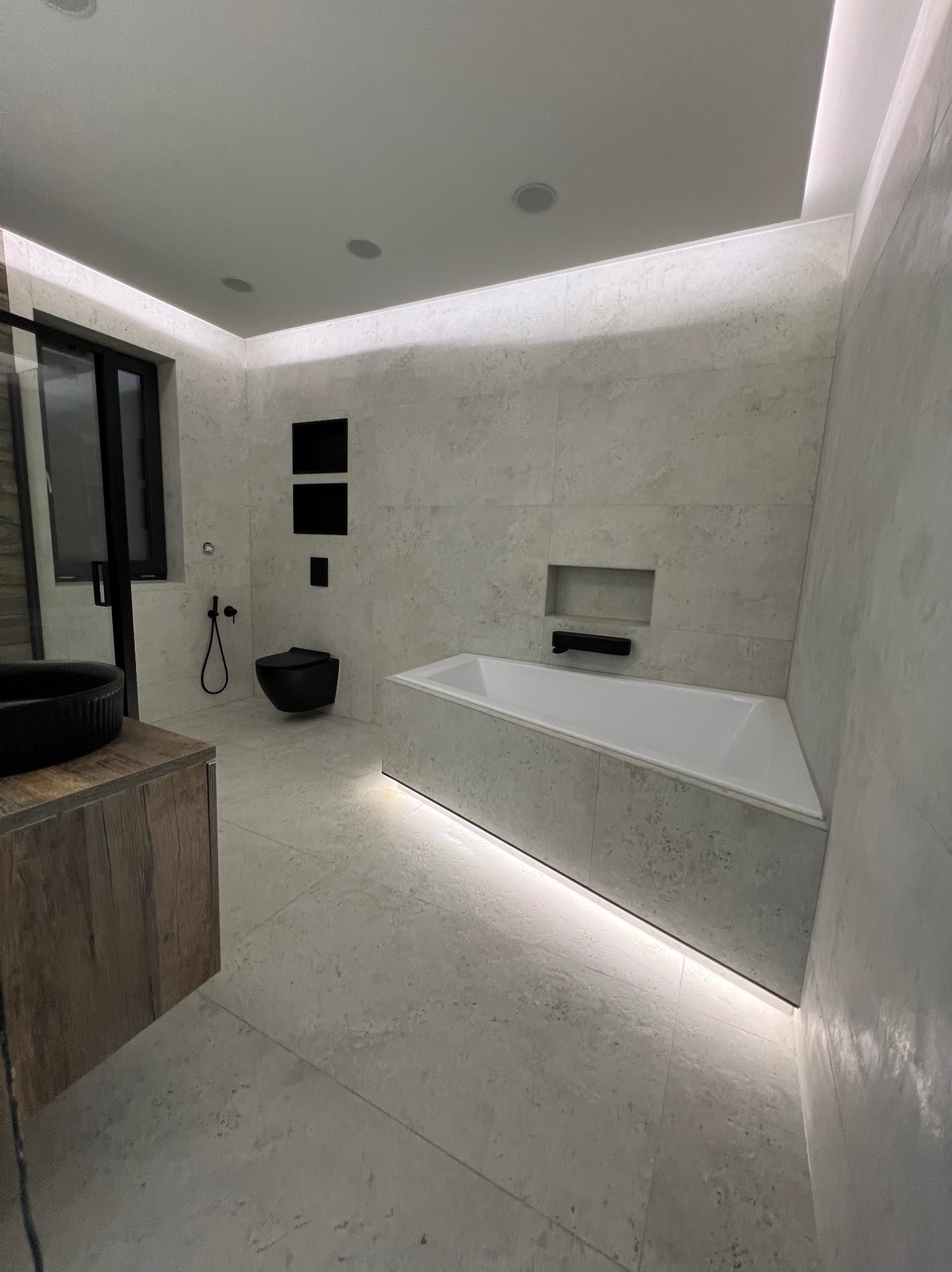 Elegancka łazienka w Zgorzelcu z podświetlaną wanną, minimalistyczną toaletą i umywalką na drewnianym blacie. Białe płytki imitujące kamień.