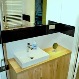 Nowoczesna łazienka z kwadratową umywalką nablatową, szafką z drewnopodobnym wykończeniem i lustrem z widocznym grzejnikiem drabinkowym w odbiciu.