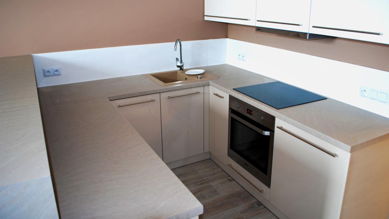 Jasna, nowoczesna kuchnia z beżowymi szafkami, blatem o fakturze drewna, płytą indukcyjną i piekarnikiem w zabudowie.