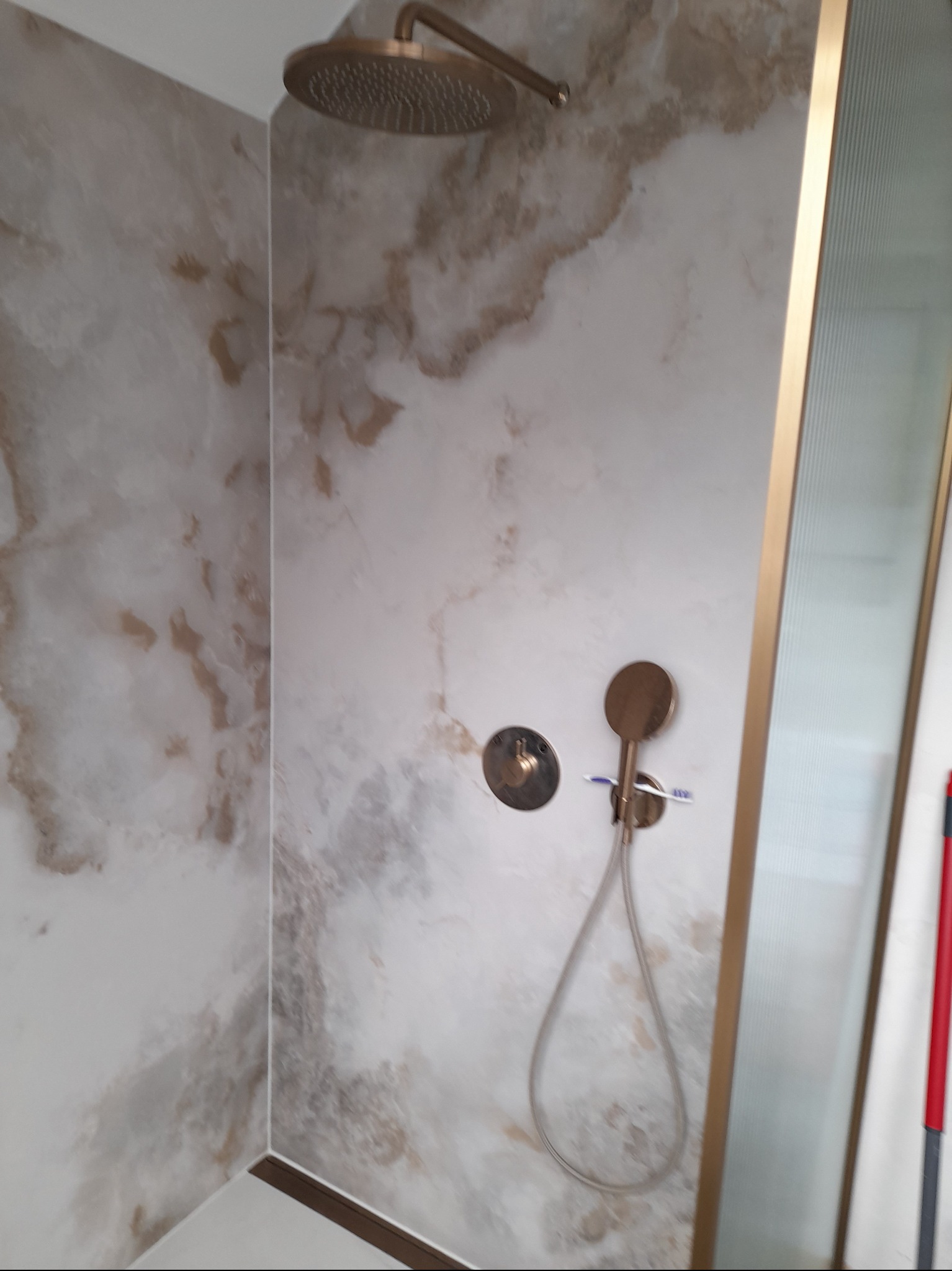 Wykończona kabina prysznicowa z deszczownicą w odcieniach beżu i złota, imitująca marmur. Widoczny panel sterowania i słuchawka prysznicowa.