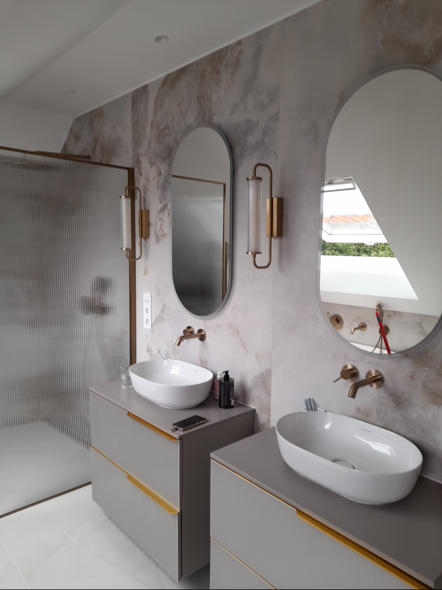 Nowoczesna łazienka z dwoma umywalkami nablatowymi, lustrami w kształcie łezki i złotymi akcentami. Kabina prysznicowa ze szkła ryflowanego. Marmurowe ściany.