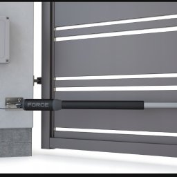 Dmytro Furyk - Szara brama wjazdowa z zamontowanym siłownikiem FORCE i skrzynką sterującą na betonowym słupku. Widok z bliska na mechanizm automatycznego otwierania.