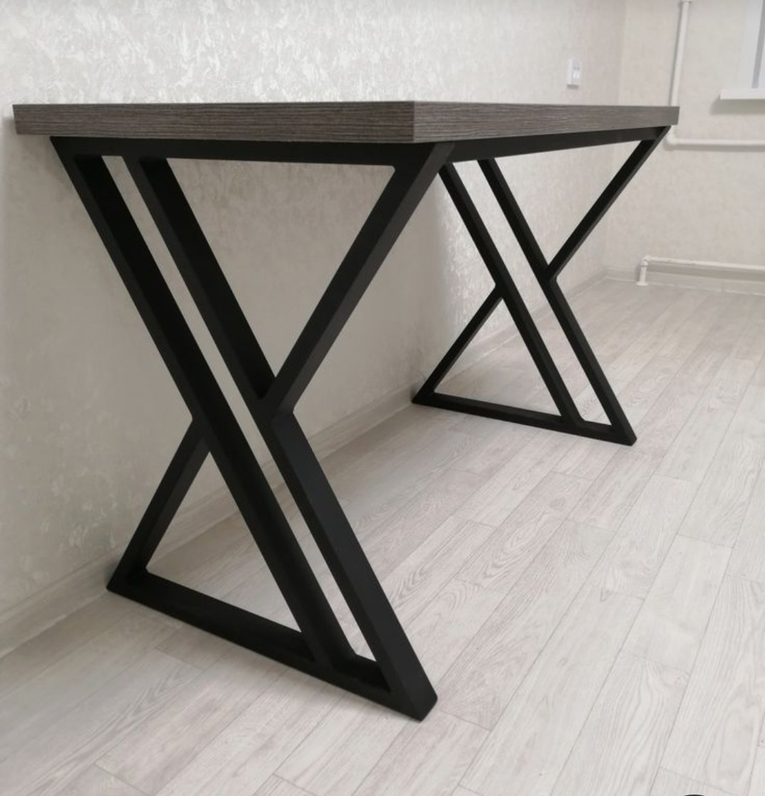 Stół z blatem imitującym drewno i czarnymi, metalowymi nogami w kształcie litery X, wykonany w Oleśnicy. Nowoczesny design, widok z boku.