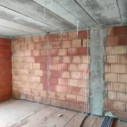 Surowy mur z instalacją elektryczną: kable, puszki, rury. Betonowy strop z przewodami. Wnętrze w stanie deweloperskim.