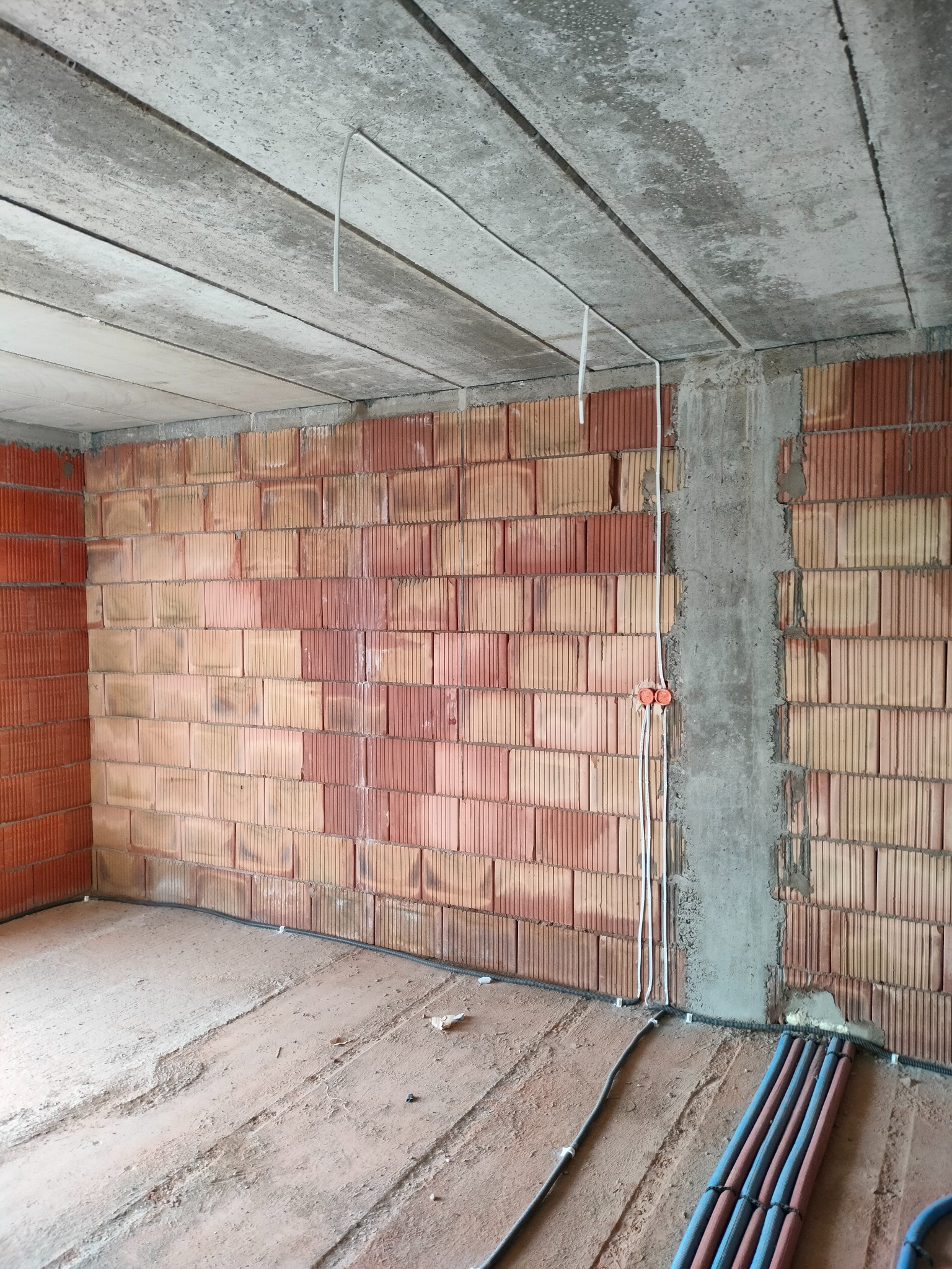 Surowy mur z instalacją elektryczną: kable, puszki, rury. Betonowy strop z przewodami. Wnętrze w stanie deweloperskim.