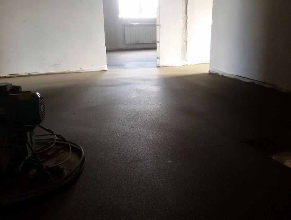 Wygładzona, ciemna posadzka jastrychowa w surowym wnętrzu, z maszyną do wygładzania w lewym dolnym rogu. Widoczne przejścia do innych pomieszczeń.