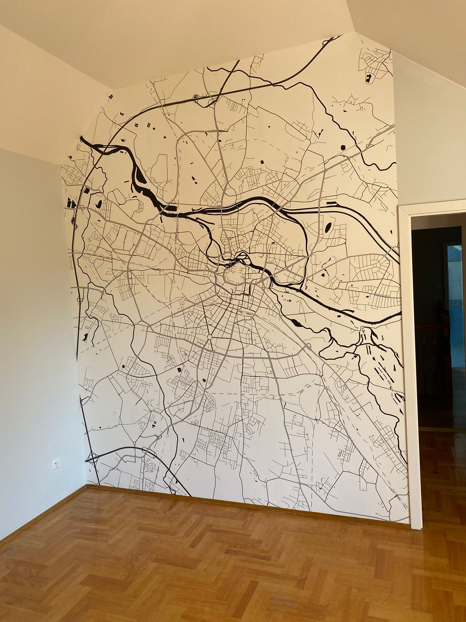 Ściana w pokoju z ręcznie malowaną mapą miasta w czerni i bieli, parkiet na podłodze. Widoczne detale mapy i precyzja wykonania.