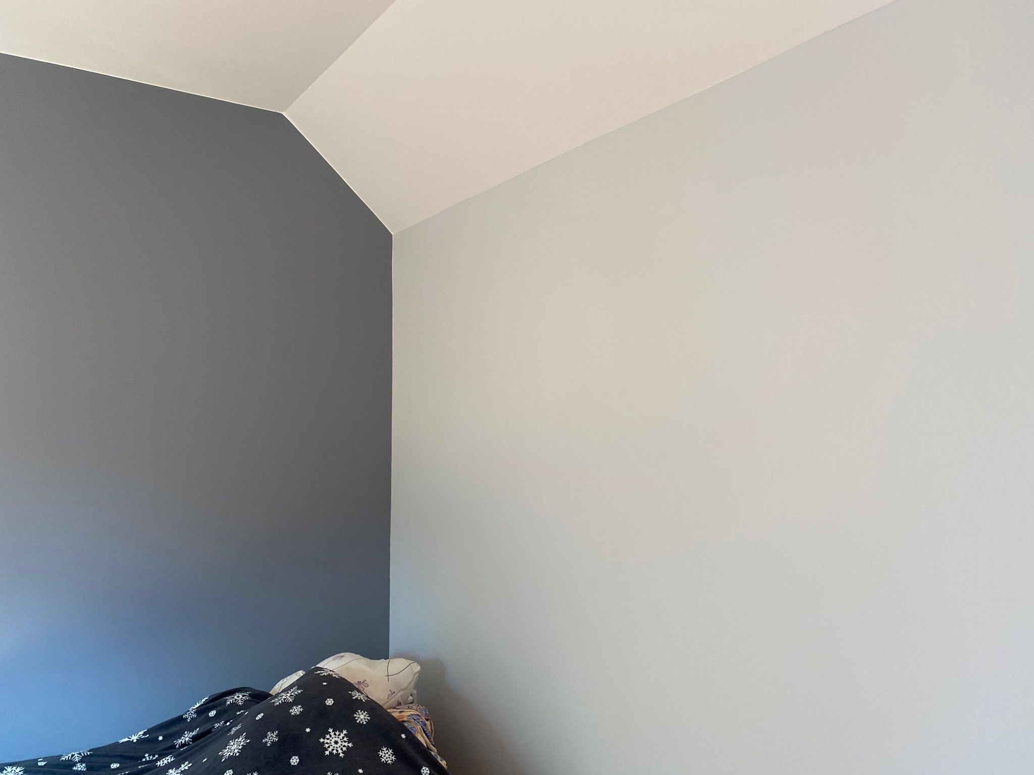 Pomieszczenie po malowaniu: szara ściana kontrastuje z jasną, podkreślając skos sufitu. W rogu widoczny fragment pościeli w śnieżynki.