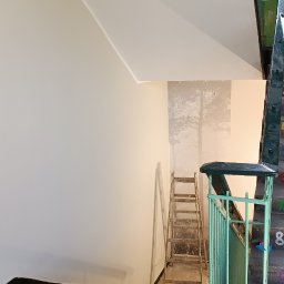 Ruslan Kostenko - Klatka schodowa w trakcie malowania: świeżo pomalowana ściana kontrastuje z fragmentem przed malowaniem. Drewniana drabina oparta o ścianę. Widoczne schody i fragment balustrady.