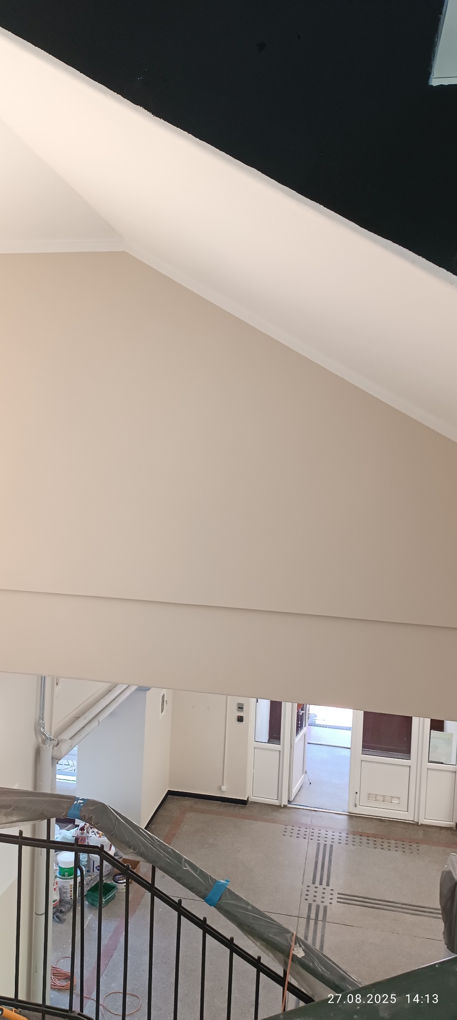 Jasne ściany po malowaniu w klatce schodowej budynku. Widoczne detale wykończenia i przygotowane narzędzia malarskie. Ujęcie z góry.