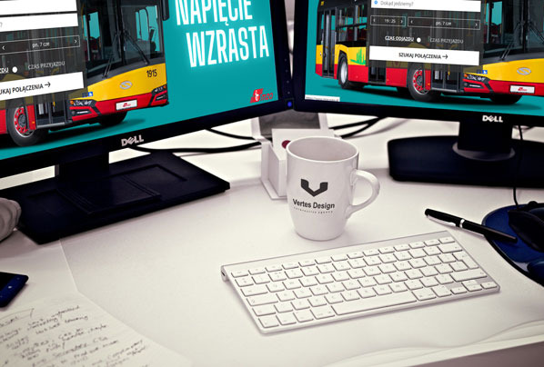 Biurko z dwoma monitorami Dell, na których widnieje strona z rozkładem jazdy autobusów. Kubek z logo firmy, klawiatura Apple i notatki na biurku.