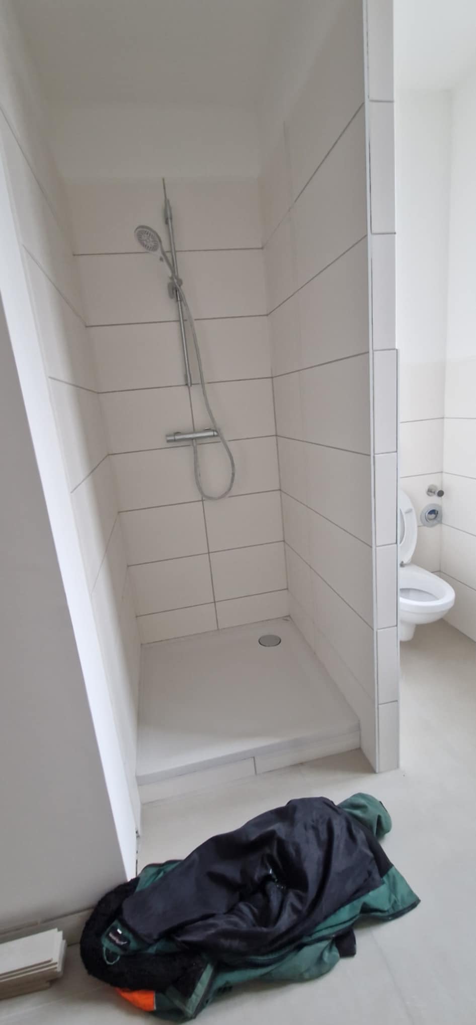 Wykończona kabina prysznicowa z białą armaturą i odpływem liniowym w Bolesławcu. Widoczna toaleta i posadzka. Minimalistyczny design z prostymi płytkami.