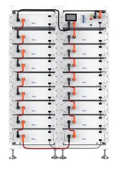 Rząd białych akumulatorów z pomarańczowymi złączami i czarnymi kablami, tworzących system magazynowania energii. Widoczny panel sterowania na górze.