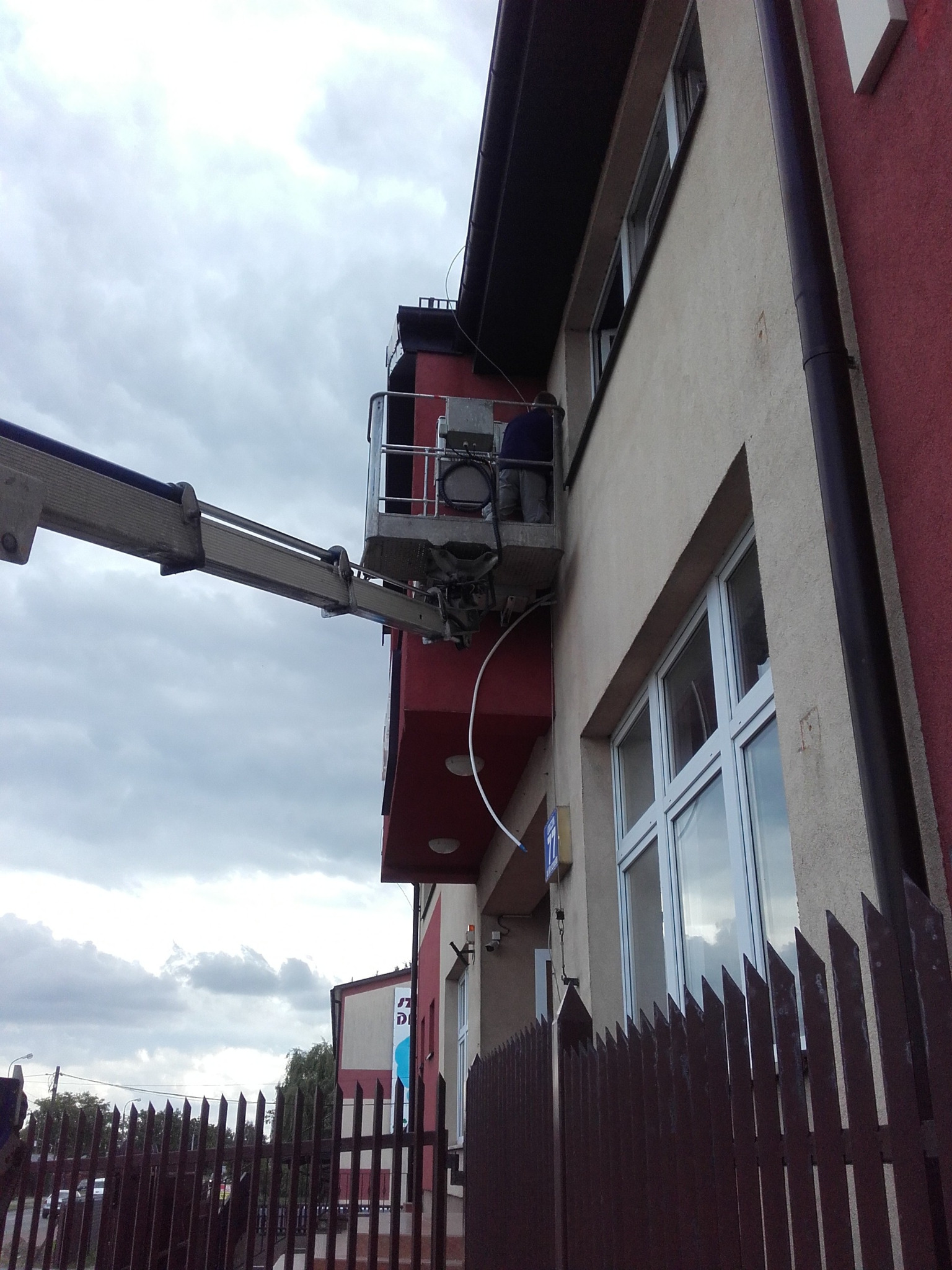 Montaż klimatyzacji na elewacji budynku z podnośnika koszowego. Widoczny pracownik w koszu i jednostka zewnętrzna klimatyzatora.